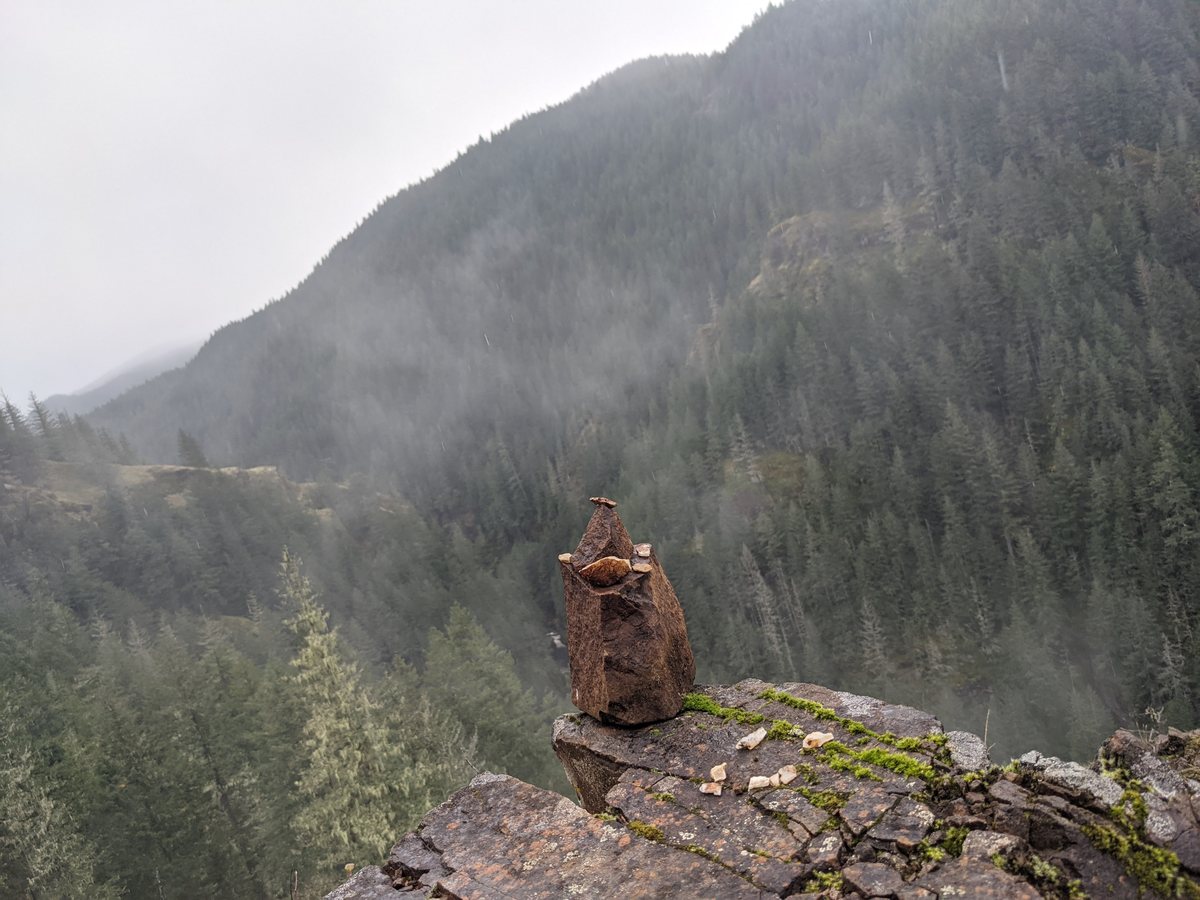 Mist over forested ridges beside a stone cairn